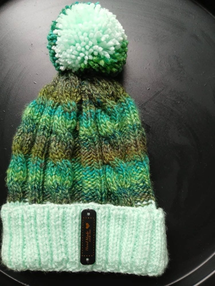 Cable-knit bobble hat in mossy green, olive and teal, with a mint cuff and a mint and green bobble