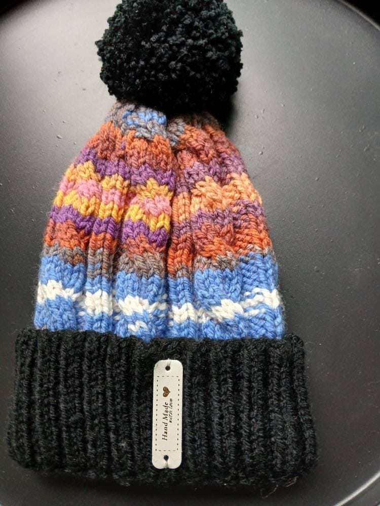 Cable-knit bobble hat striped blue, orange, violet and mustard, with a black cuff and black bobble