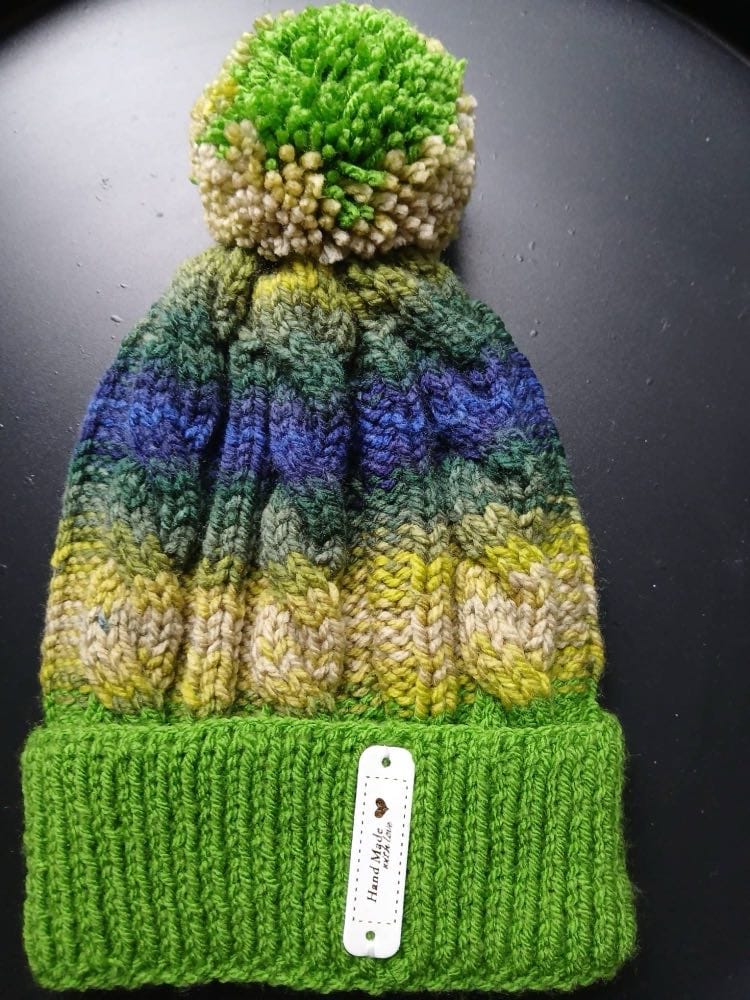 Cable-knit bobble hat striped sand, olive, forest green and blue, with a grass-green cuff and a green and sand bobble